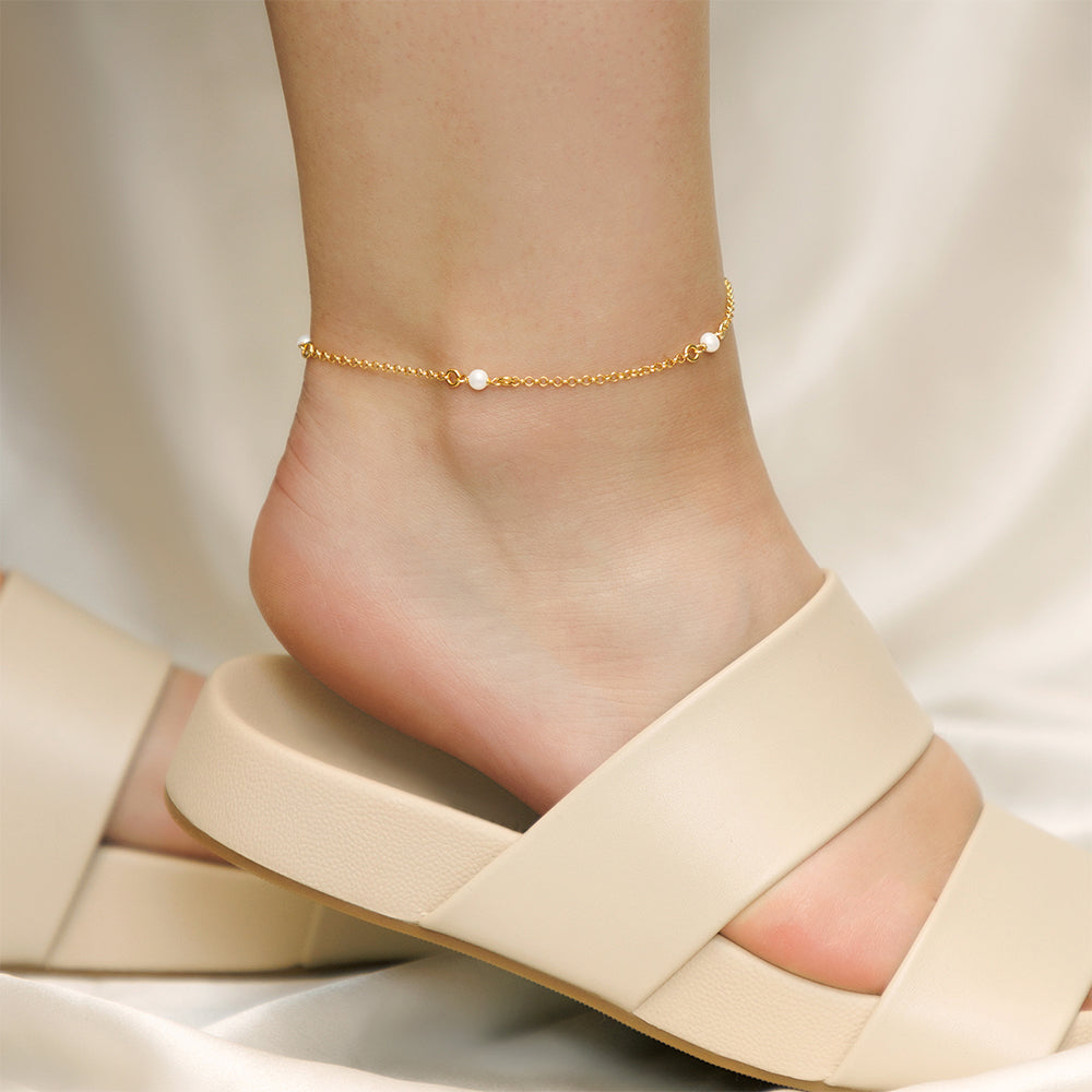 A sterling silver anklet adorned with gold-plated pearl charms, gracefully adorning a woman's leg.