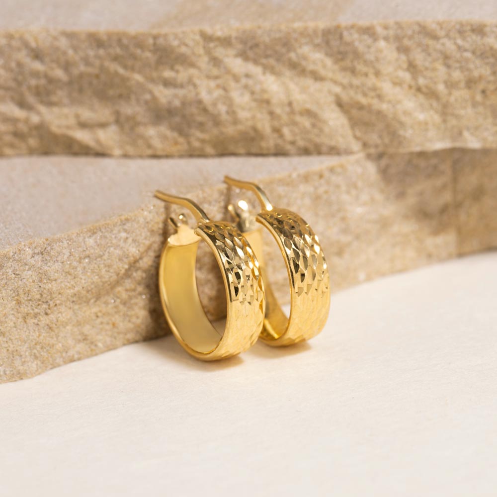 Close-up of elegant gold hoop earrings against a warm sandy background.