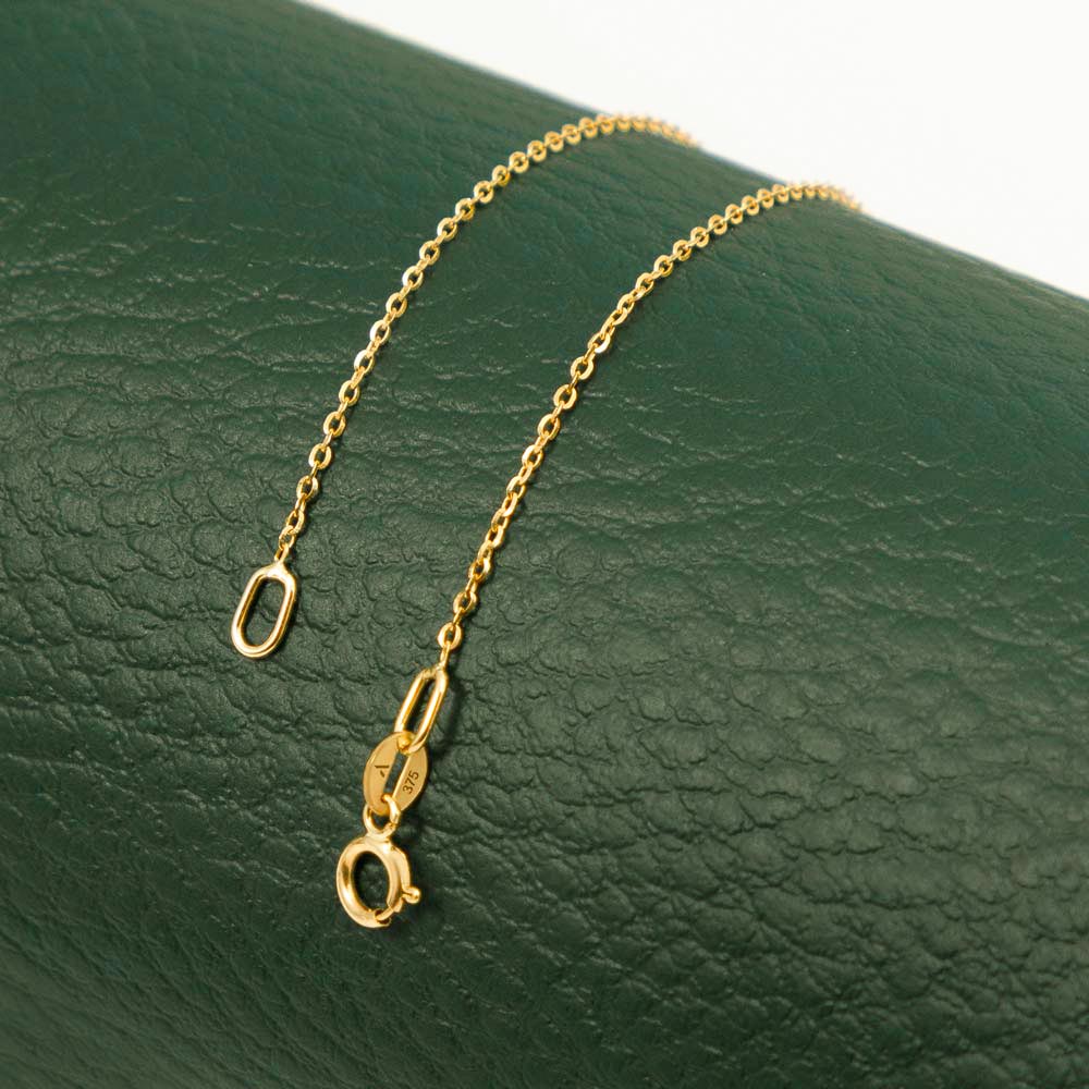 Close-up of a thin gold chain elegantly captured against a vibrant green background.