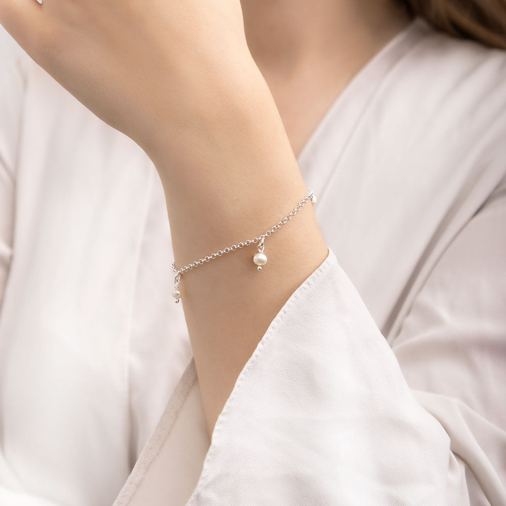 A silver bracelet elegantly adorned with round pearl charms, gracefully showcased on a woman's hand against a clean white background.