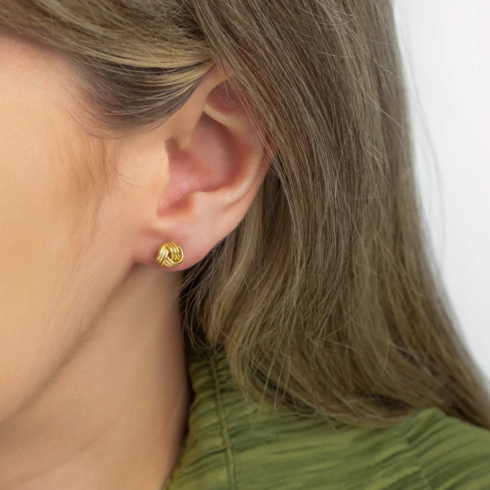 Close up picture of a woman wearing gold knot studs earring