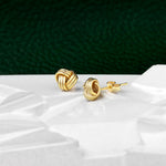 Chic gold knot stud earrings placed on a white marble with a contrasting dark green background