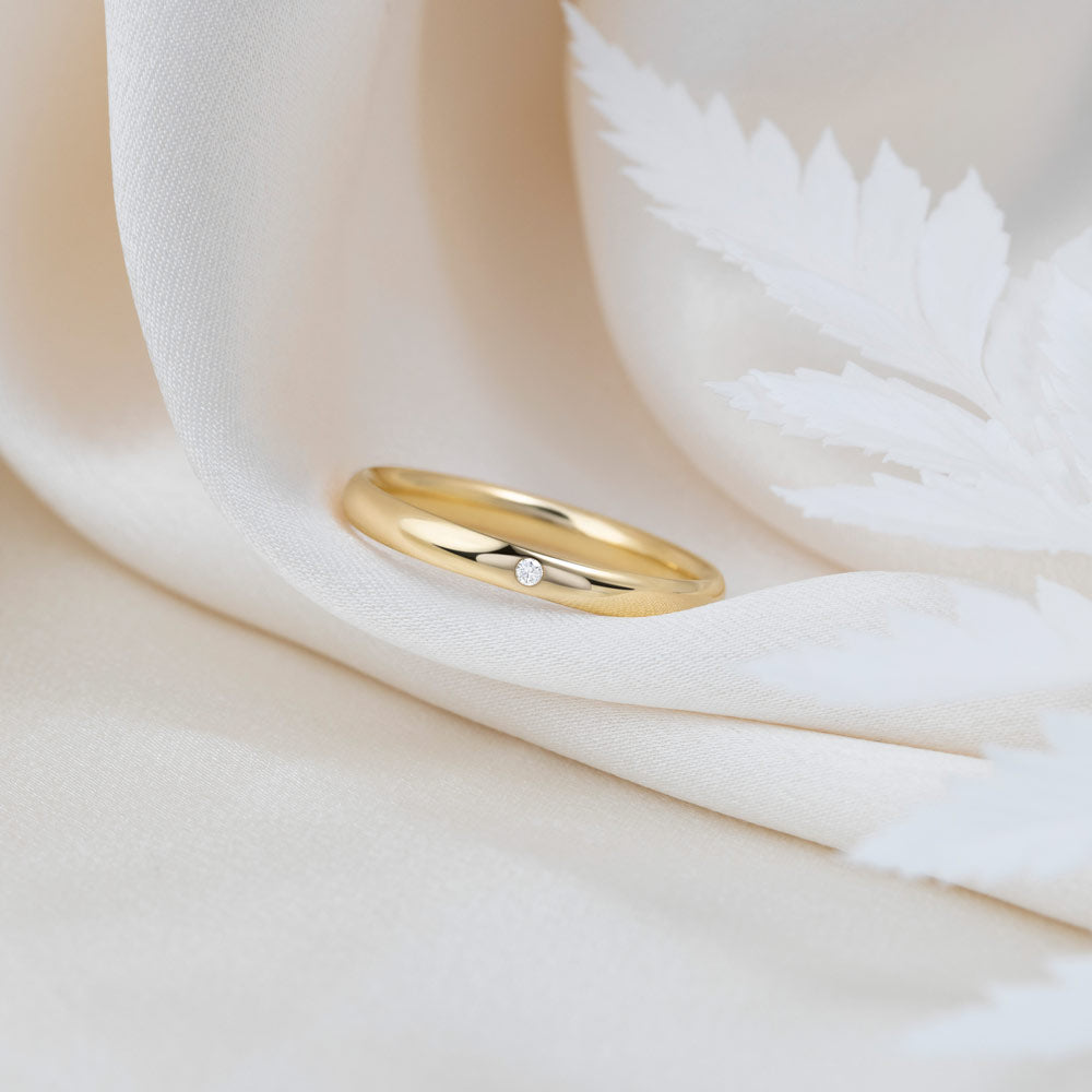 A 9ct gold wedding band with 1.3 mm cubic zirconia stone placed on a beige fabric background