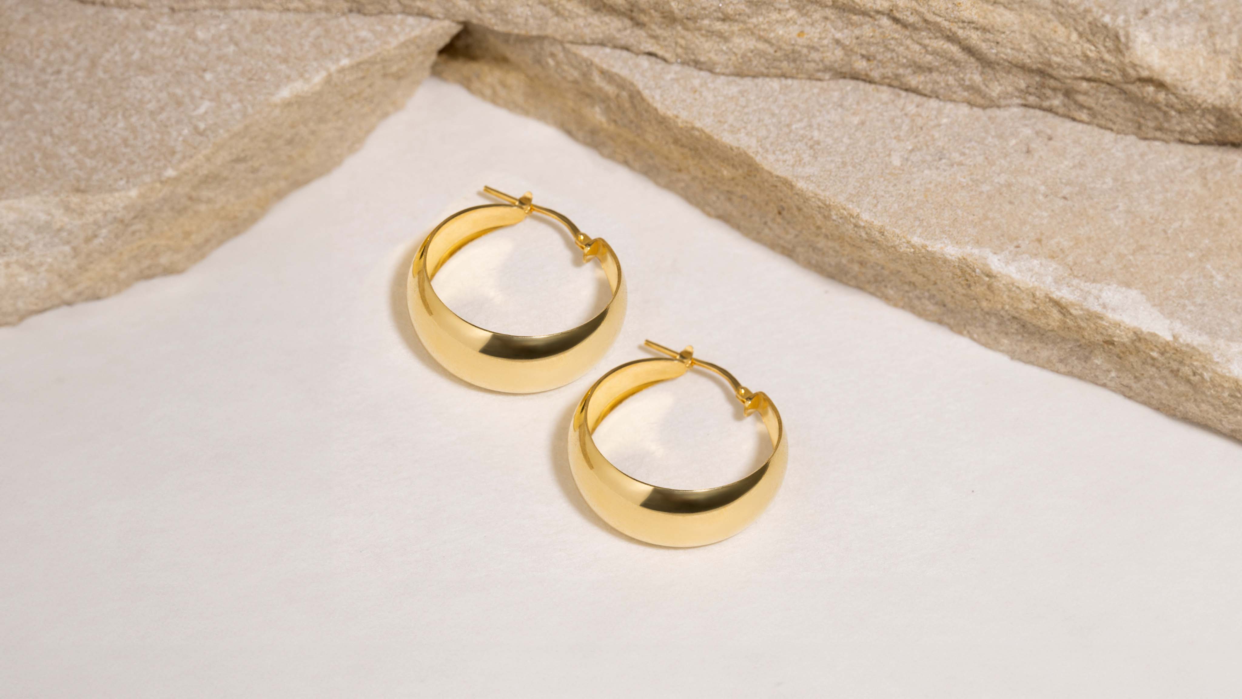 Close-up of elegant gold hoop earrings against a warm sandy background.