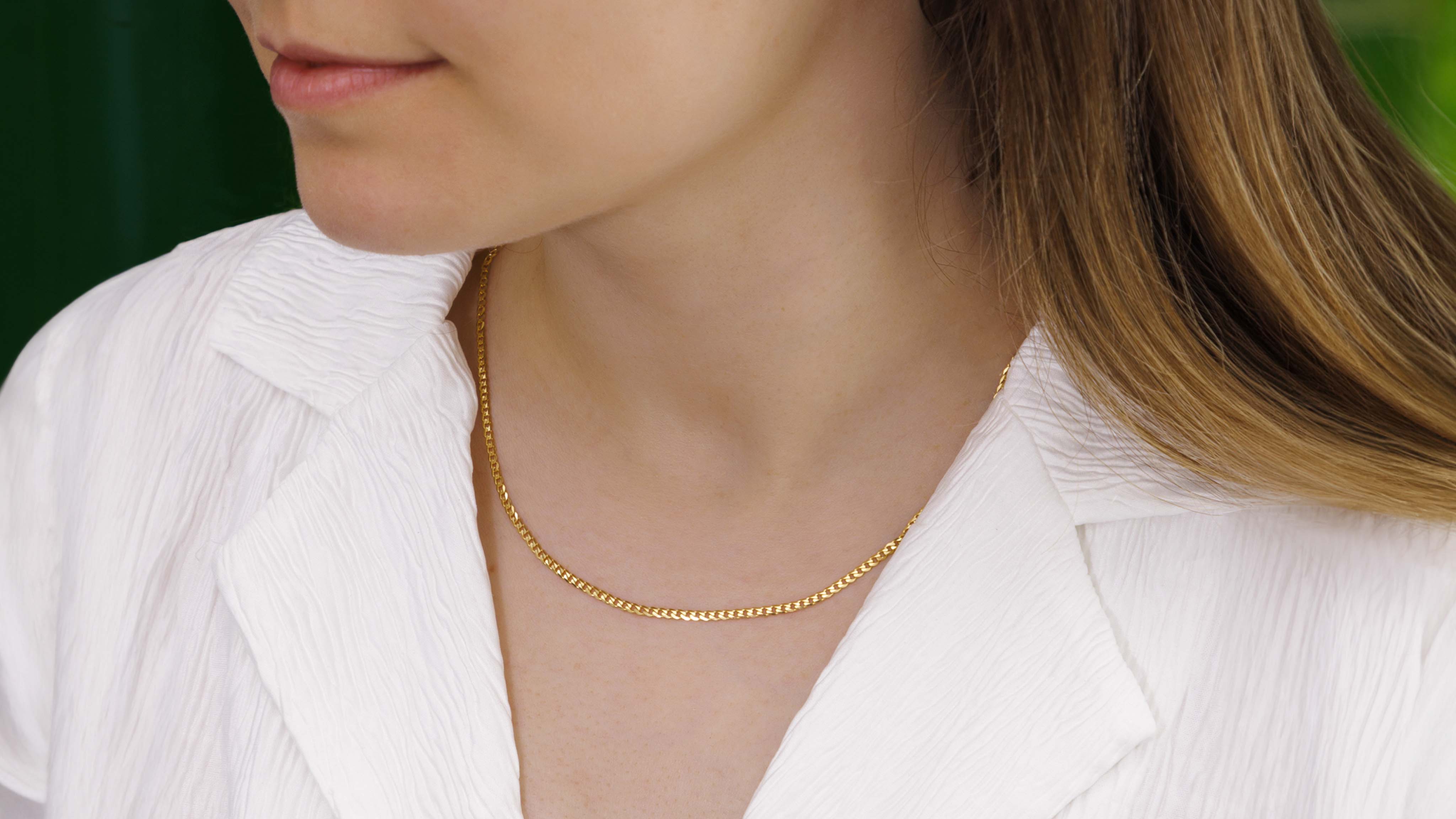 Close-up of a thin gold chain elegantly captured against a vibrant green background.