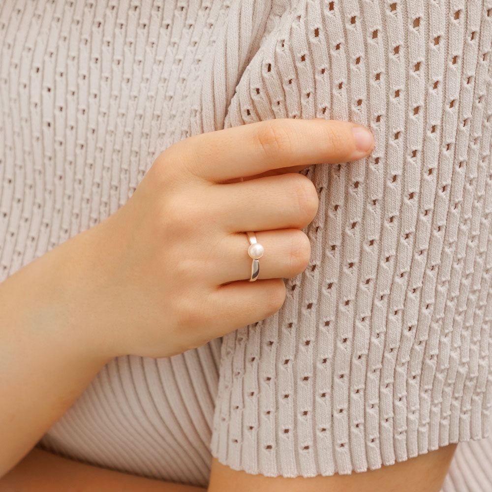 Silver ring with pearl on a woman's hand against beige t-shirt.  