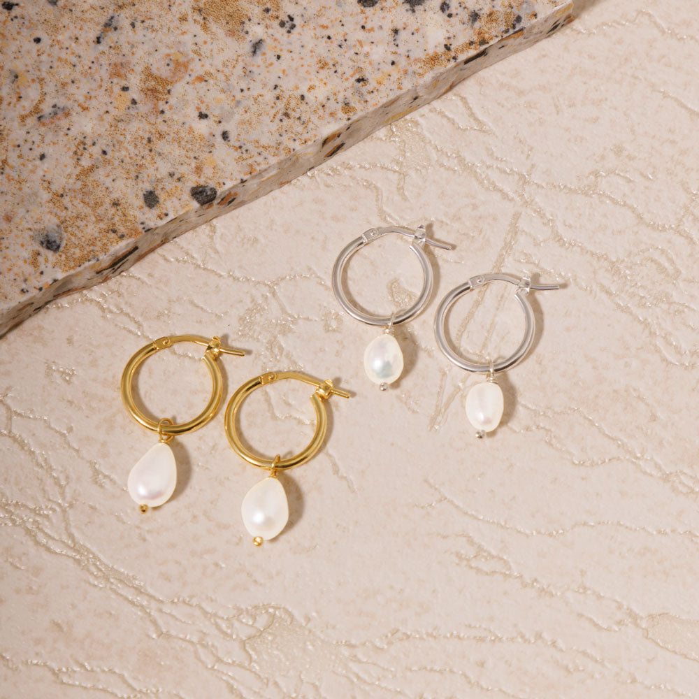 Two sets of beautifully crafted earrings, each with round design and pearl, displayed on a textured sand tile background.