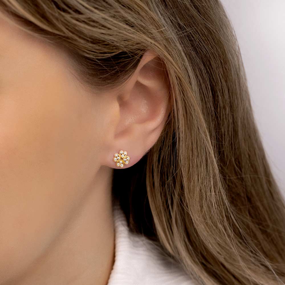 A picture of a woman wearing gold clover Studs with cubic zirconia stones