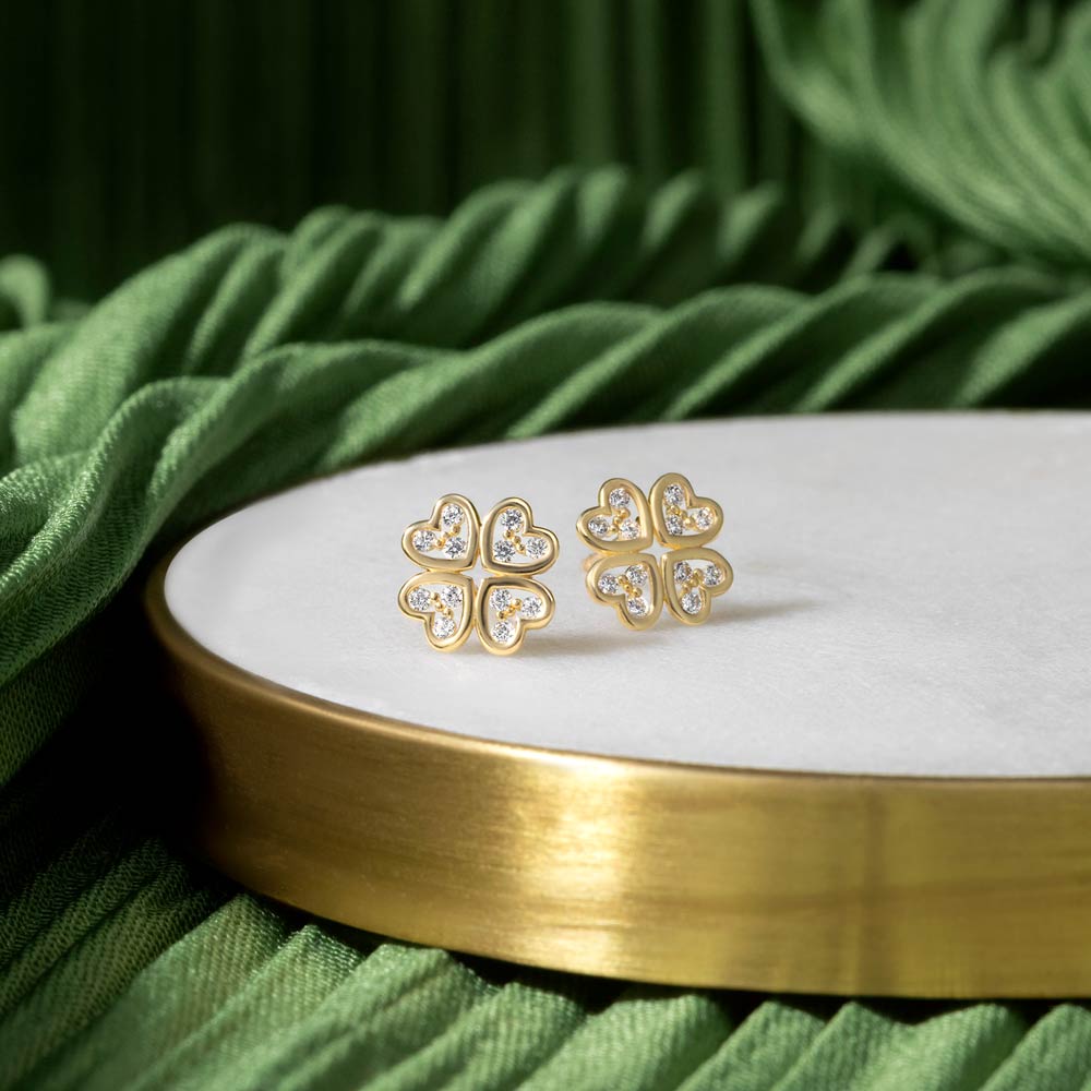 Gold clover Studs with cubic zirconia stones placed on a white and green background 