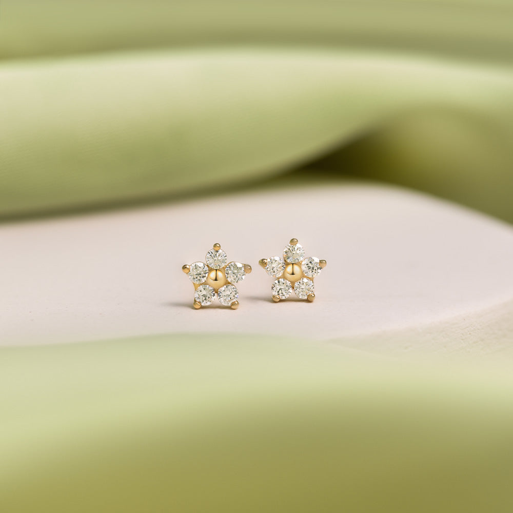 Pair of 9K gold flower studs presented on a white stone against green details.