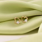 Pair of 9K gold heart studs presented on a white stone against green details.