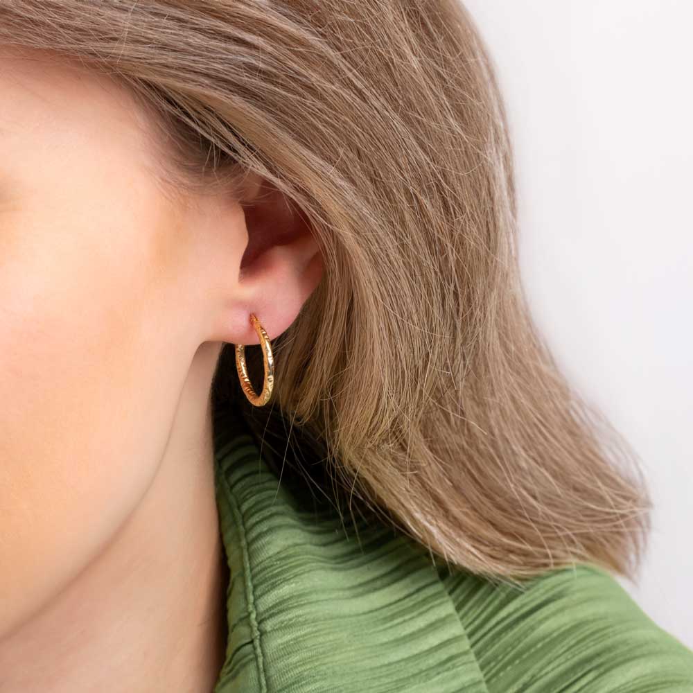 Close up picture of a woman wearing Gold Hammered hoop earrings