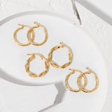 Three pairs of gold twisted hoops earrings placed on a concrete white surface