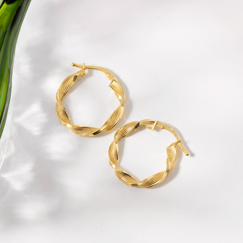 Elegant gold hoop earrings placed beside a green glass vase