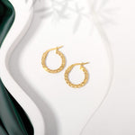 Gold twisted hoops earrings placed on a white surface