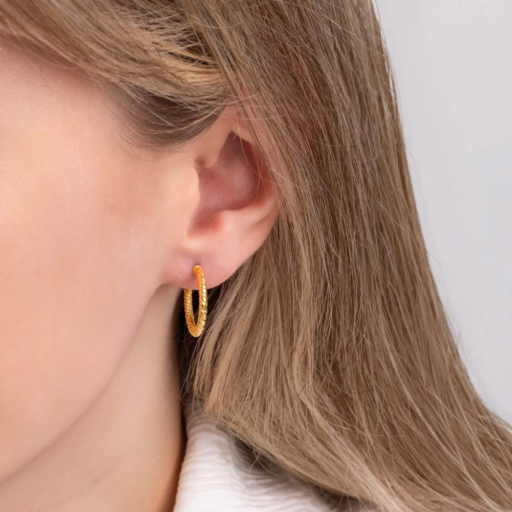 Close up picture of a woman wearing rope pattern hoop earrings