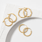 Three pairs of gold twisted hoops earrings placed on a concrete white surface