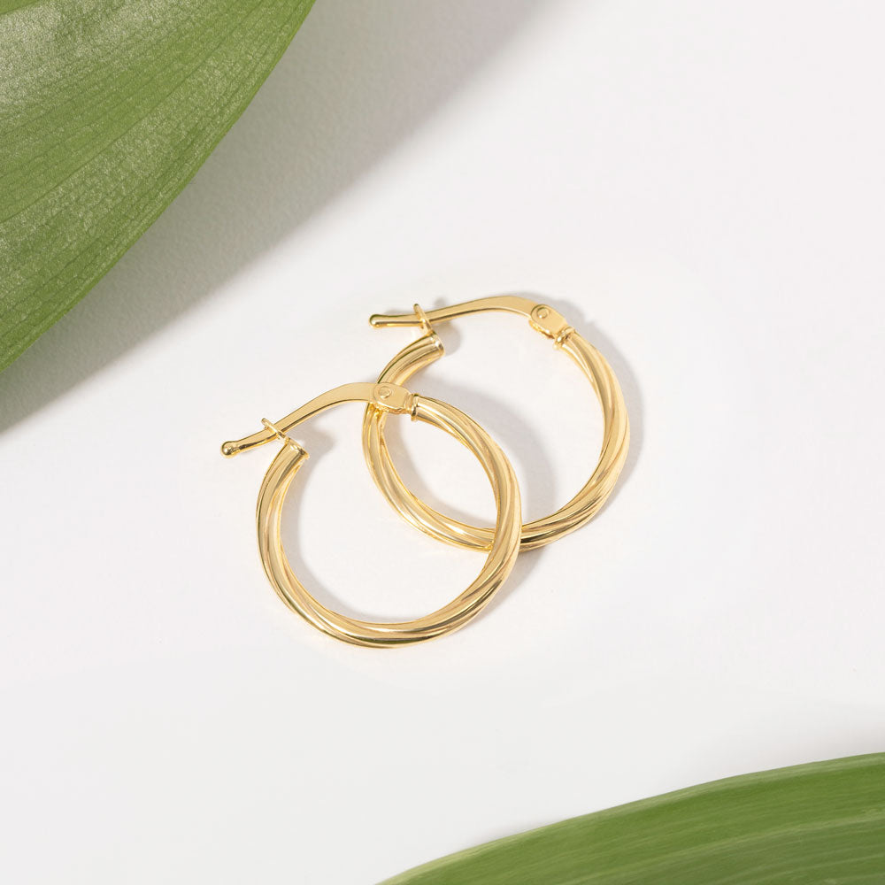 Gold twisted hoops earrings resting next to a green leaf