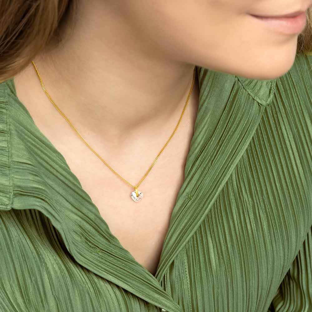 Woman wearing 9ct gold Heart crystal pendant against green blouse. 