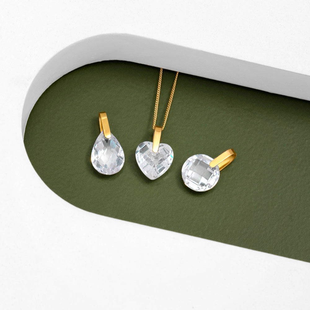 An image showing three 9ct gold crystal pendants Waterdrop shape Heart shape and Round shape placed on a green and white background.