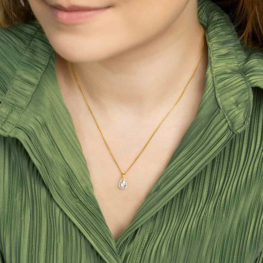 Woman wearing 9ct gold Waterdrop crystal pendant against green blouse. 