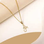 A delicate gold necklace is pictured with an alphabet pendant in the form of the letter 'A' resting on a cream-colored surface