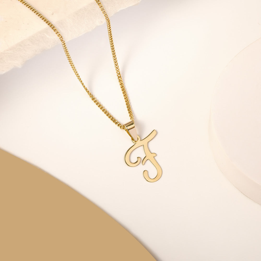 A delicate gold necklace is pictured with an alphabet pendant in the form of the letter 'F' resting on a cream-colored surface