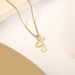 A delicate gold necklace is pictured with an alphabet pendant in the form of the letter 'F' resting on a cream-colored surface