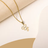 A delicate gold necklace is pictured with an alphabet pendant in the form of the letter 'G' resting on a cream-colored surface