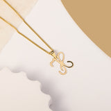 A delicate gold necklace is pictured with an alphabet pendant in the form of the letter 'H' resting on a cream-colored surface