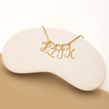 A gold necklace with a chain featuring four hanging alphabet initials: H,I,J,K. The necklace is displayed on a curved, white stand