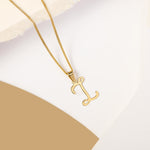 A delicate gold necklace is pictured with an alphabet pendant in the form of the letter 'I' resting on a cream-colored surface