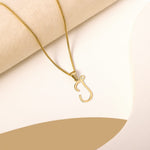 A delicate gold necklace is pictured with an alphabet pendant in the form of the letter 'J' resting on a cream-colored surface