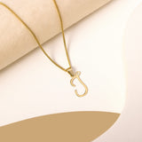 A delicate gold necklace is pictured with an alphabet pendant in the form of the letter 'J' resting on a cream-colored surface