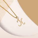 A delicate gold necklace is pictured with an alphabet pendant in the form of the letter 'K' resting on a cream-colored surface