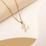 A delicate gold necklace is pictured with an alphabet pendant in the form of the letter 'L' resting on a cream-colored surface