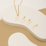 A display showcasing gold letter pendants: a letter 'L' pendant on a necklace on a scalloped base and individual alphabet pendants 'O', 'V,' and 'E' 