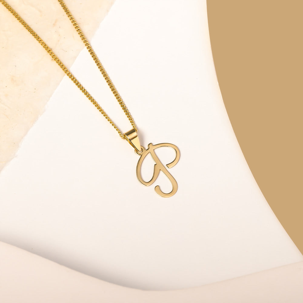 A delicate gold necklace is pictured with an alphabet pendant in the form of the letter 'P' resting on a cream-colored surface