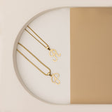 A minimalistic display of two gold necklaces, each featuring an alphabet pendant in the shape of a stylized letter "P" and "R"