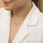 A woman wearing a gold necklace with an alphabet pendant in the shape of the letter 'R'. The text in the corner notes, "Note: Chain not included.