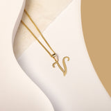 A delicate gold necklace is pictured with an alphabet pendant in the form of the letter 'V' resting on a cream-colored surface