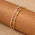 a pair of gold plated and silver paperclip bracelets placed on a brown roll