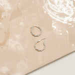 Marketing image of Silver Polished Twisted Hoops with post notch againts beige-brown tile.