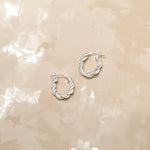 Marketing image of Silver Oval Polished Twisted Hoops with post notch againts beige-brown tile.