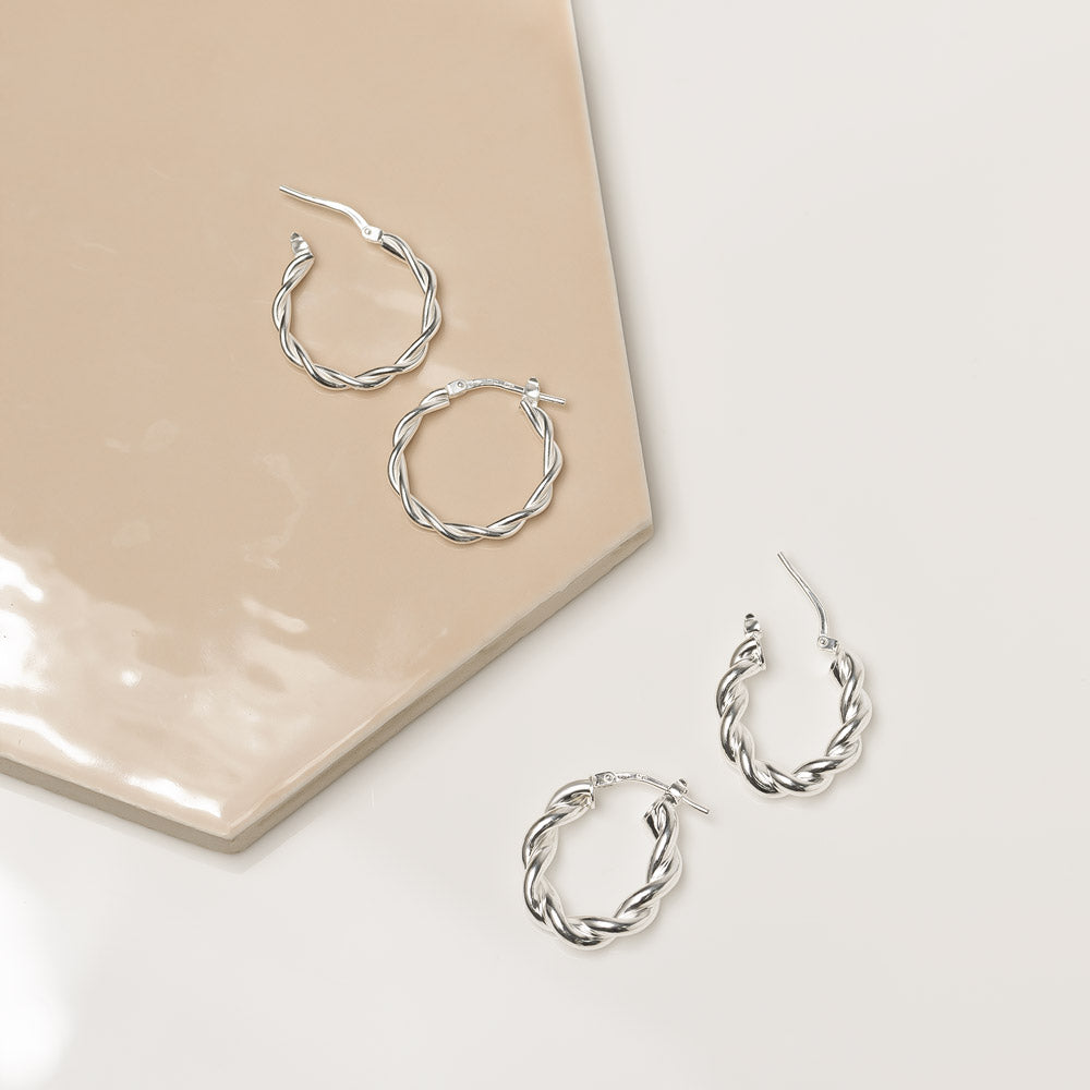 Marketing image of Silver Polished and Silver Oval Polished Twisted Hoops with post notch againts beige-brown tile.