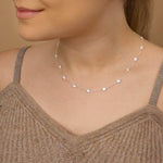 A woman wearing silver CZ charm necklace around her neck in brown top