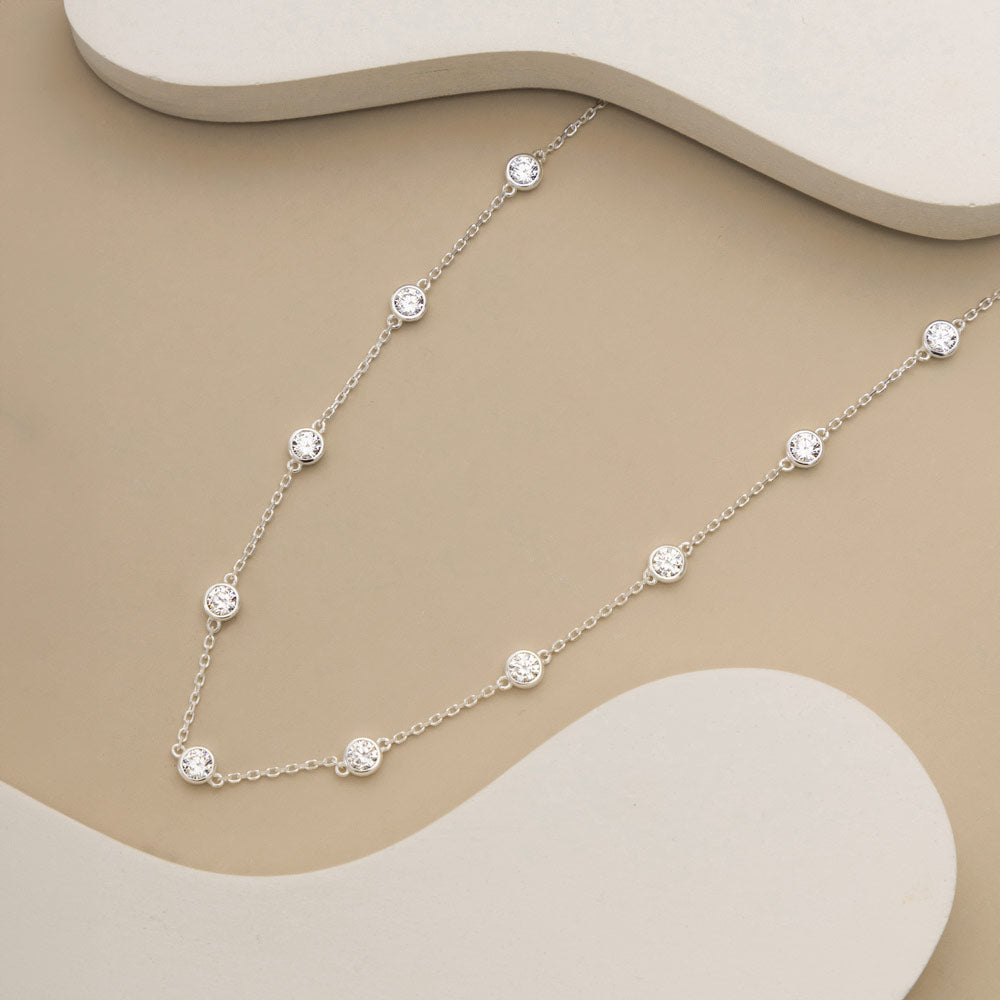 An image showing silver CZ charm necklace placed on a beige and white background