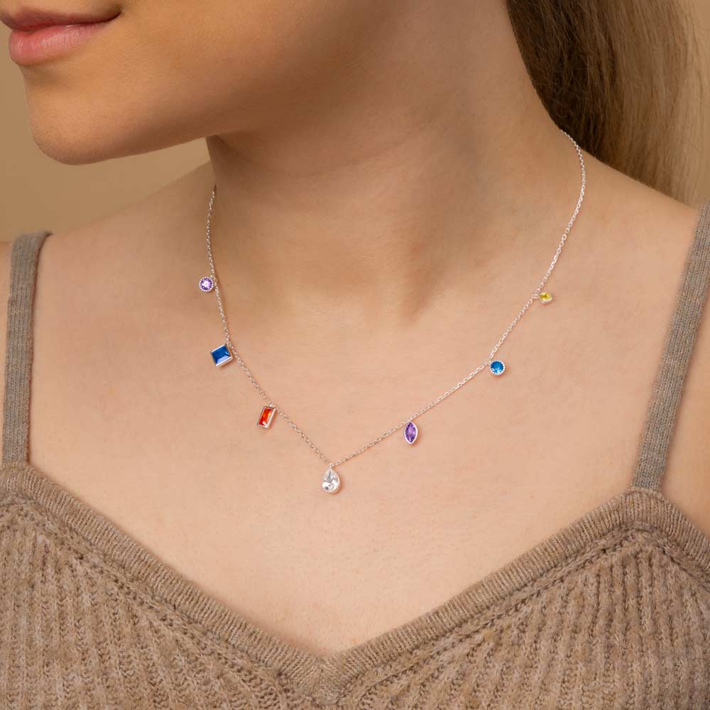 A woman wearing silver rainbow multi shapes hanging charm pendant necklace around her neck in brown top