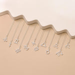 Twelve zodiac necklaces placed one next to each other against beige background and white details.