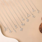 Twelve zodiac necklaces placed one next to each other against beige background and white details.